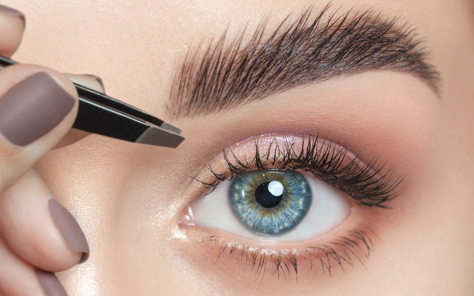 Brow shaping with tweezers beside defined lashes